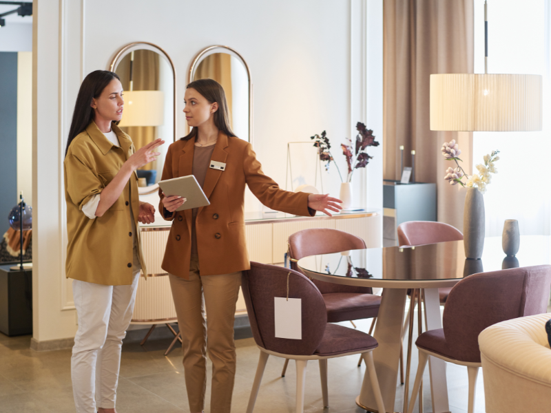 A manager with a tablet showing new pieces of furniture to a customer