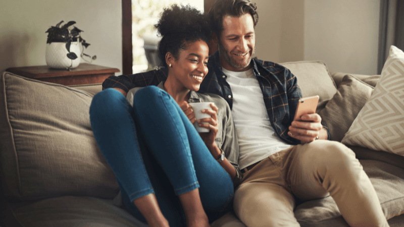 happy young couple using a digital tablet while relaxing on a couch in their living room at home