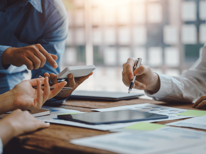 Close-up of hands collaborating over documents and devices at a meeting table.