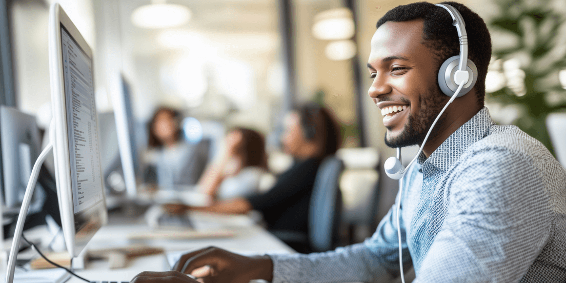 A man with a headset smiling while using a computer in an office.