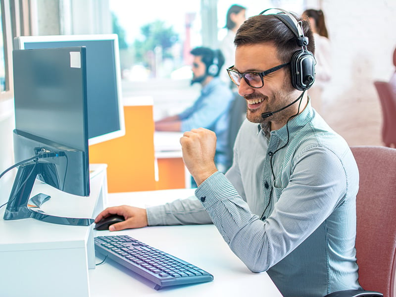 Contact center employee smiling as he talks to a customer on a headsetter smiling