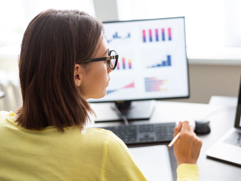 woman wearing glasses looking at graphs on computer screen