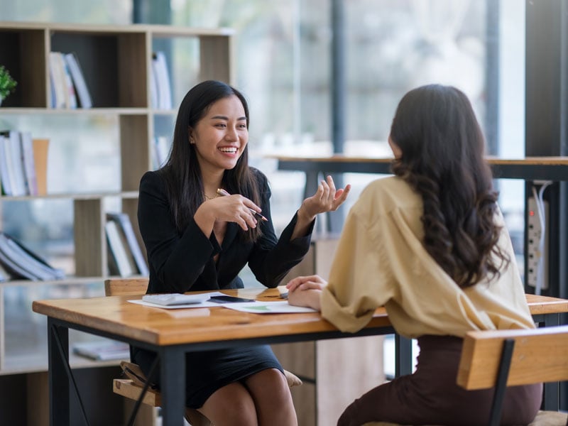 two female employees in office chatting at a desk