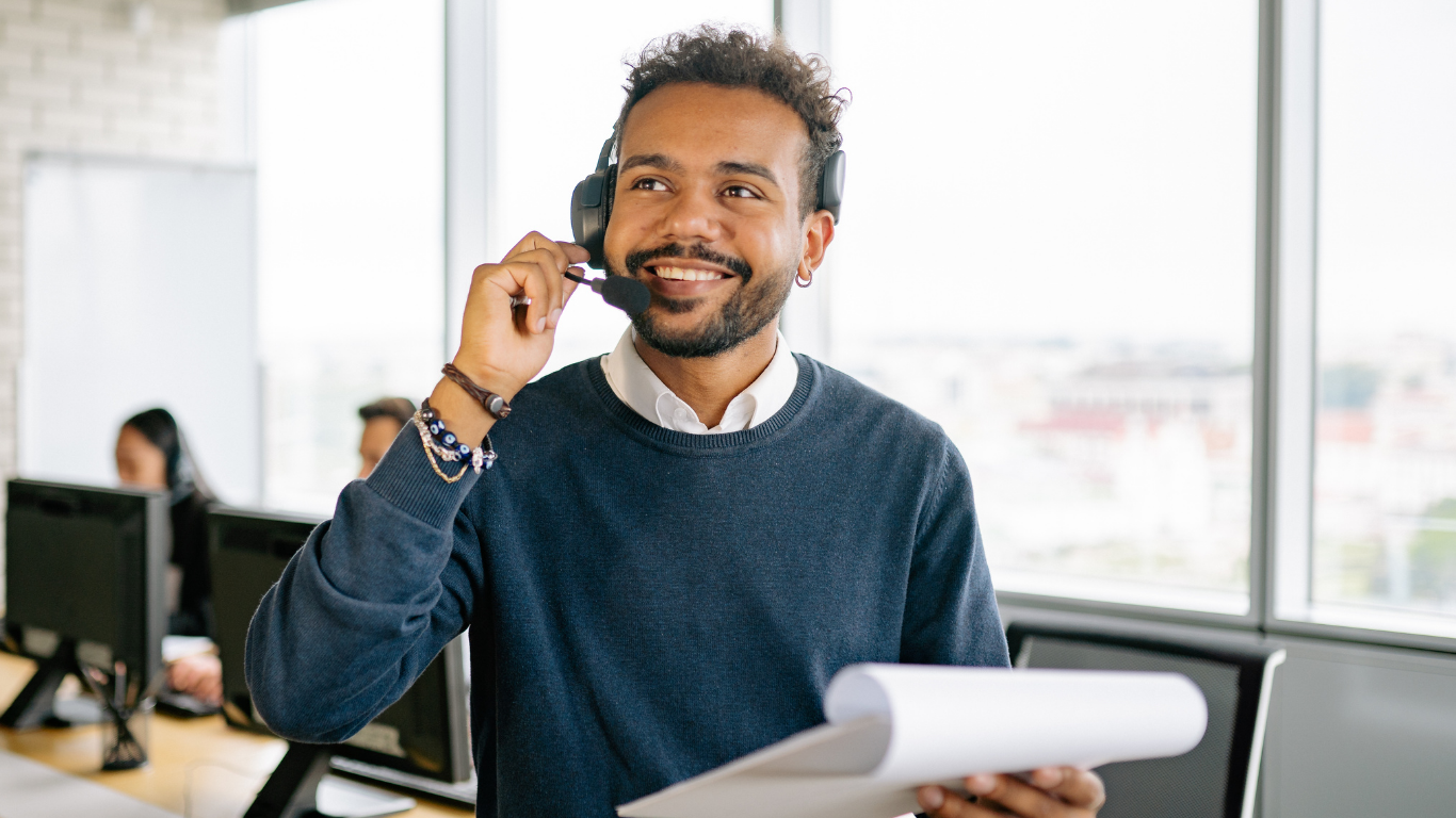 Contact center agent smiling while taking a customer call at a desk with a notepad 