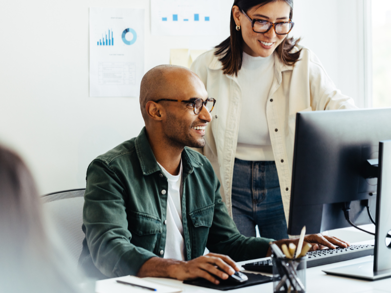 Two coworkers smiling while working together at a computer.