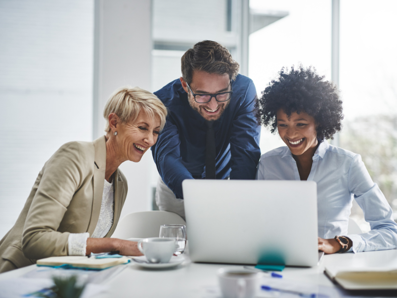 A group of three professionals smiling and gathered around a laptop.