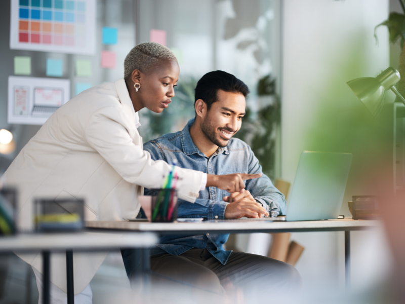 A woman pointing at a laptop screen while working with a colleague.