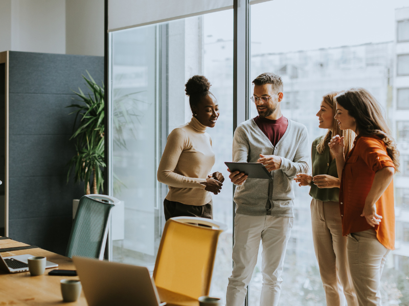 A group of four people standing and discussing something on a tablet.