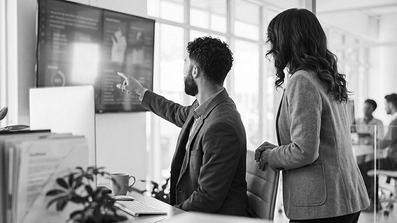 Two business professionals analyzing customer experience data and insights displayed on a large screen in a bright, collaborative office environment.