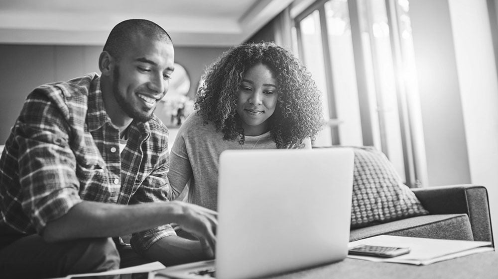 A couple is smiling while using a computer at home.