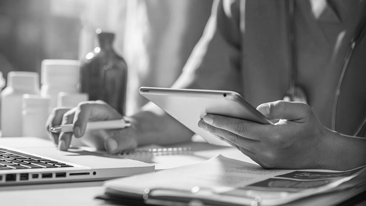 A doctor is focused on using a laptop while holding a tablet in their other hand.