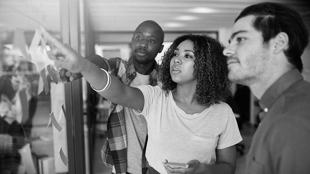 A diverse team of consultants collaboratively reviewing and prioritizing journey insights on a glass wall, driving alignment around key customer experience improvements.
