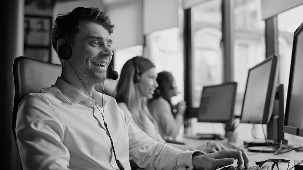 A smiling agent communicates via a headset while working in a call center office.
