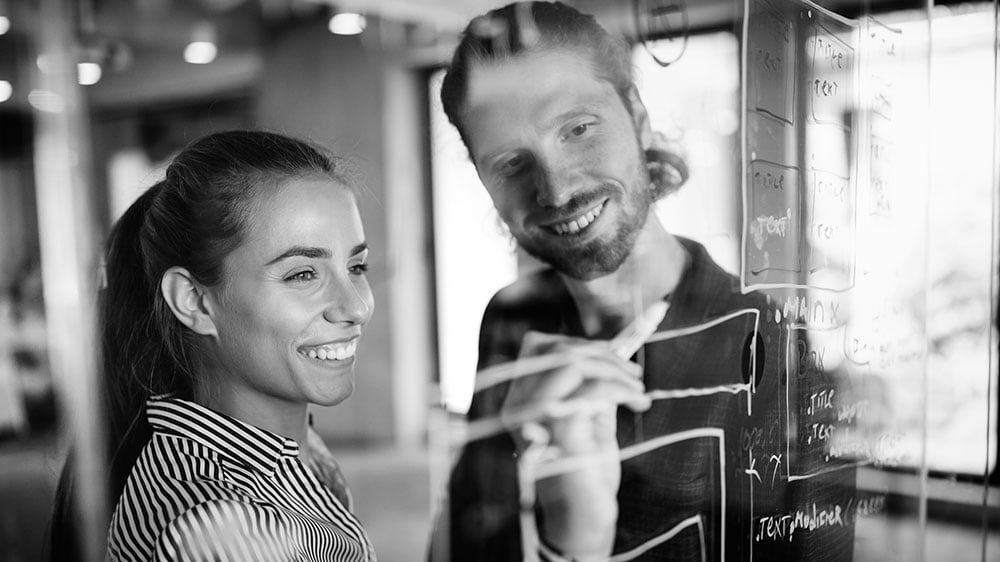 Two consultants are co-designing a digital solution framework on a glass surface.