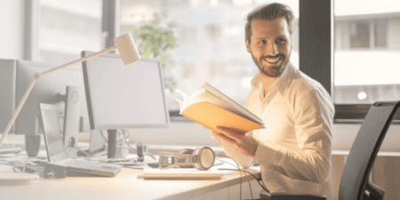 Happy man sitting at his desk holding an open notebook