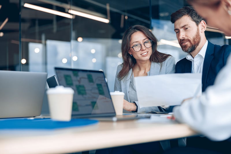 Two financial professionals reviewing documents and laptop data during a collaborative meeting in a modern office setting