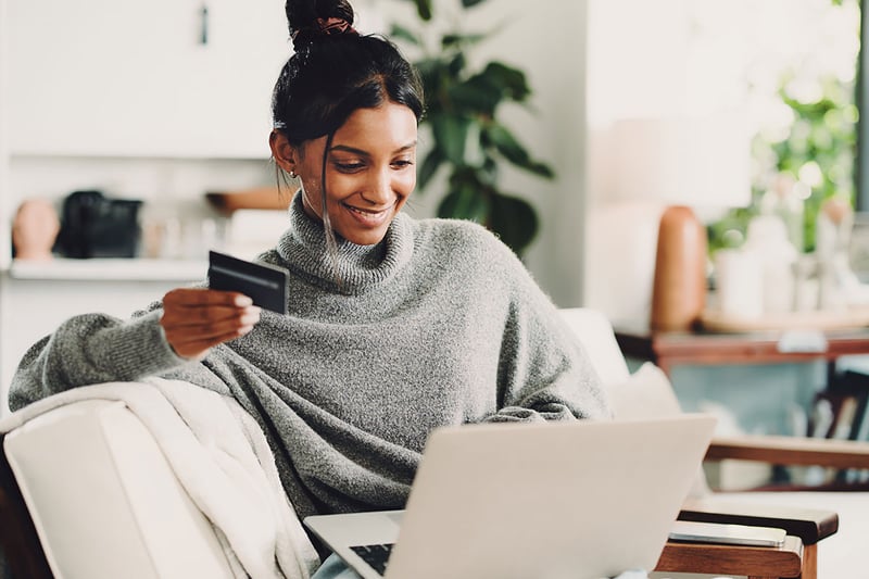 A woman shopping online, using her laptop and credit card to complete her purchase.