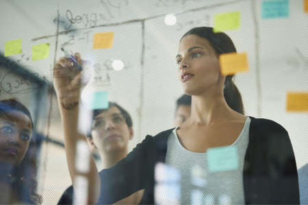 Woman drawing on a glass board with others watching