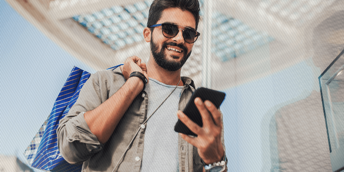 Young man walking out of a store holding shopping bags and using their mobile phone