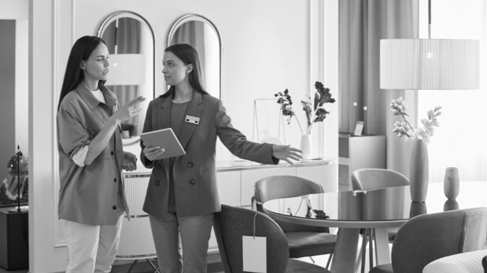 A manager with a tablet shows new pieces of furniture to a customer.