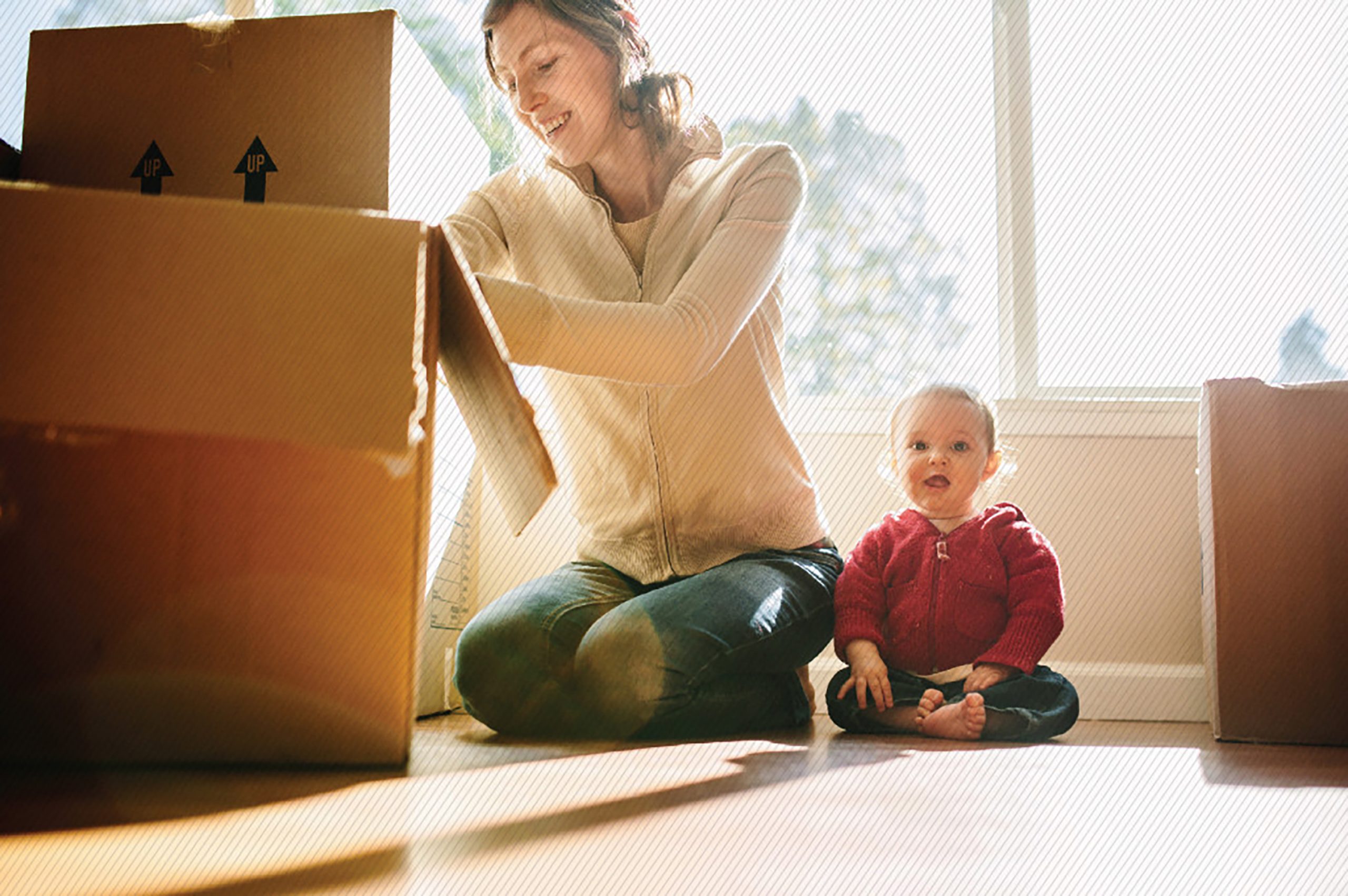 A mom unpacking boxes with her toddler sitting next to her
